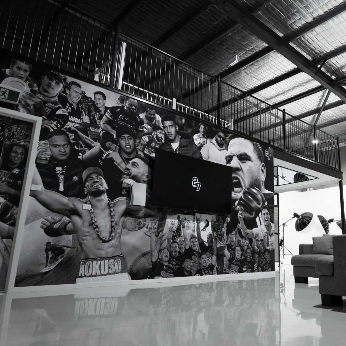 A modern indoor space featuring a large wall mural with various portraits, a mounted flat-screen TV, and a gray sofa.