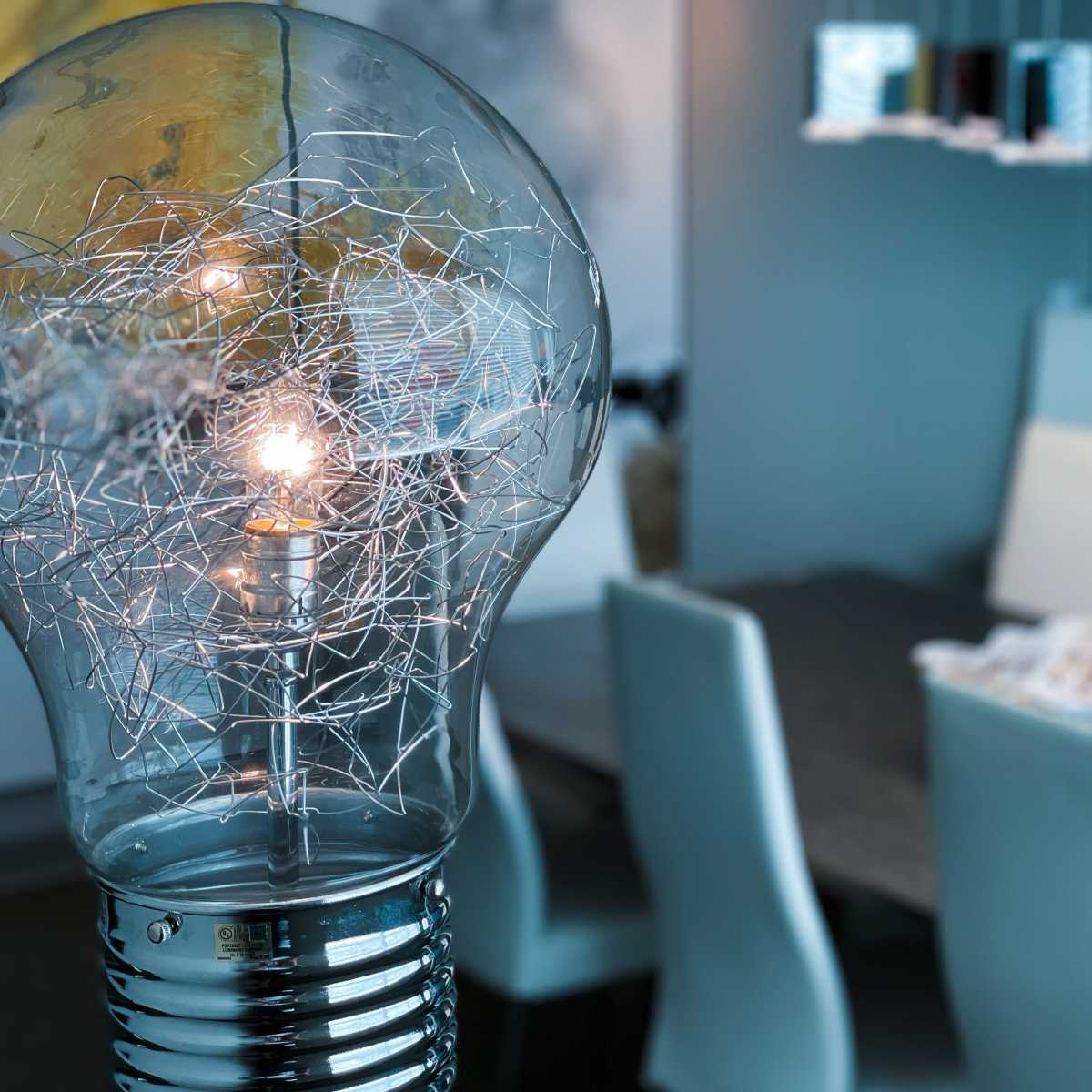 A decorative light bulb with visible filament illuminates a modern dining area featuring a table and white chairs.