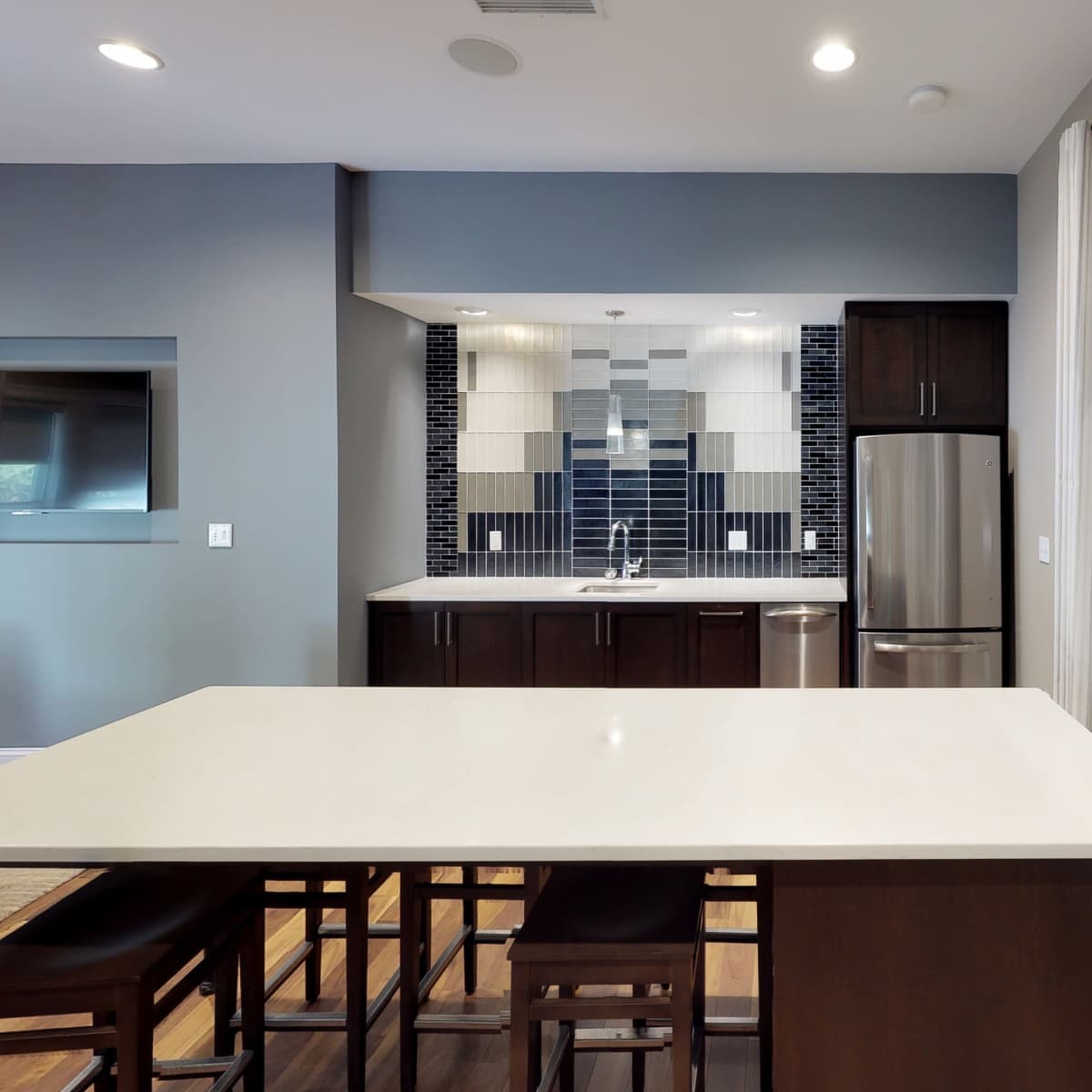 A modern kitchen features dark wooden cabinets, stainless steel appliances, and a large island with seating.