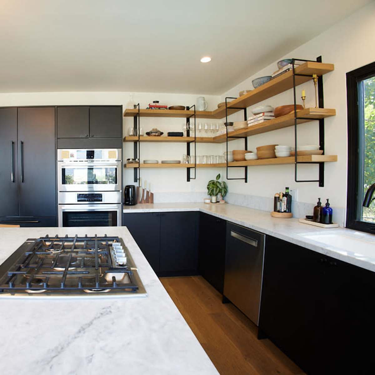 A modern kitchen featuring a marble countertop, black cabinetry, open shelving with dishware, and stainless steel appliances.