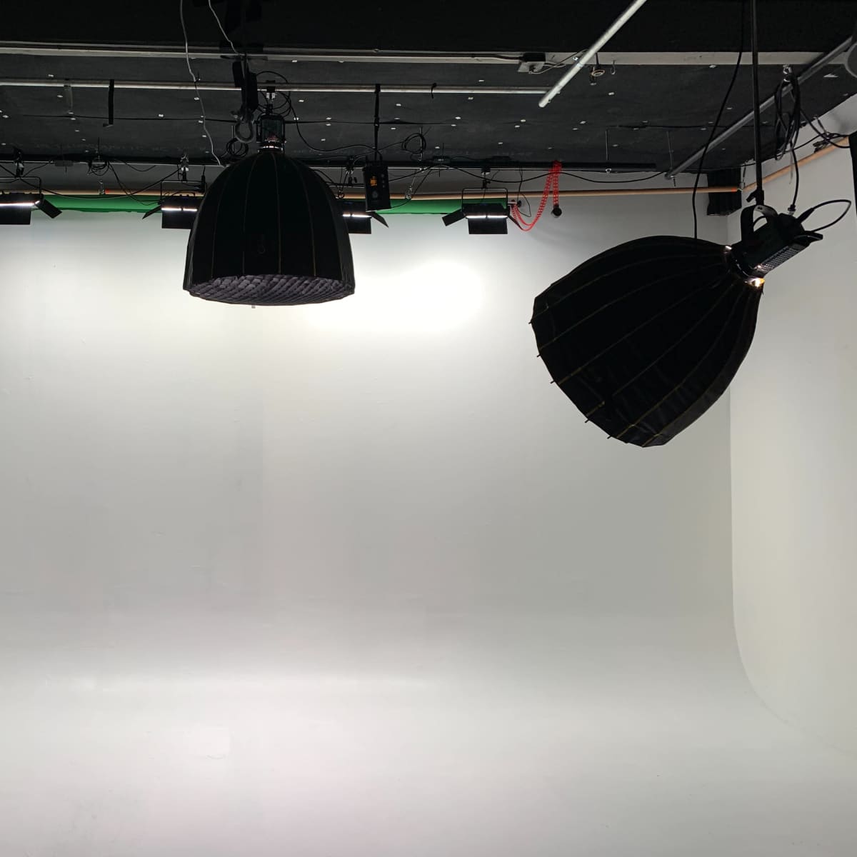 A sparsely furnished photography studio with a white backdrop, two hanging lights, and black curtains.