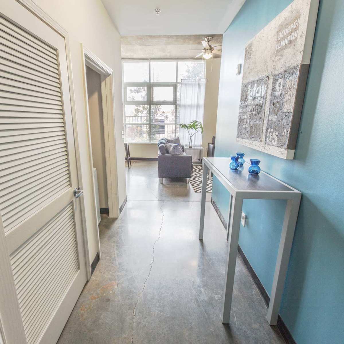 A hallway leading to a living area, with a console table against a blue wall and a closed door on the left.
