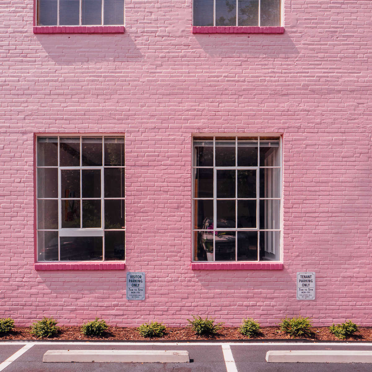 A pink brick wall with four square windows and two signs near the bottom.