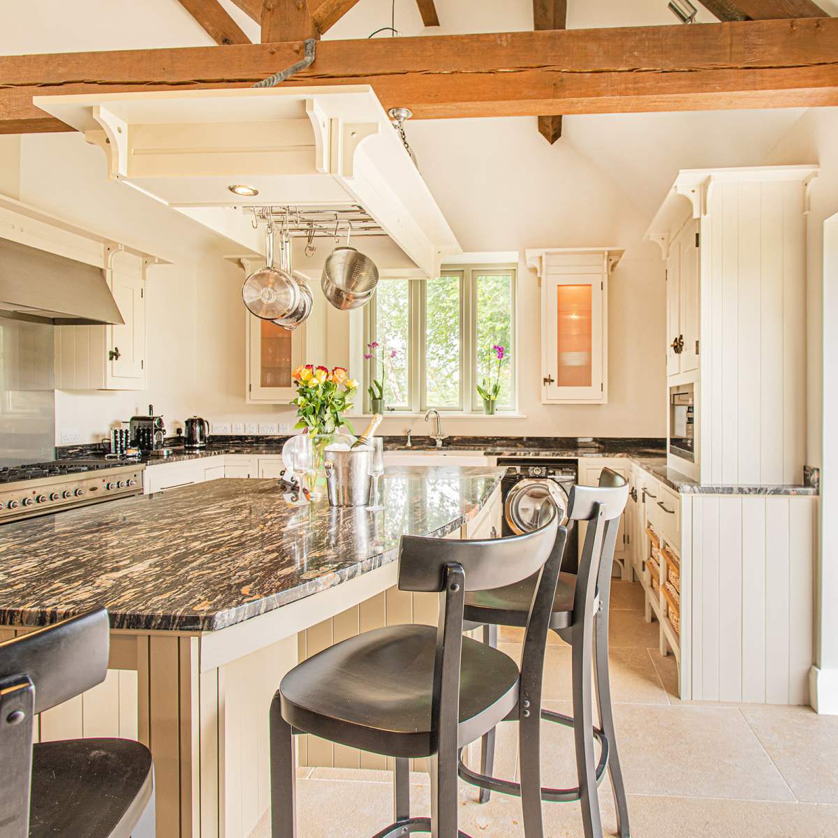 A modern kitchen features a large island with bar stools, stainless steel appliances, and opens to a stone patio through glass doors.