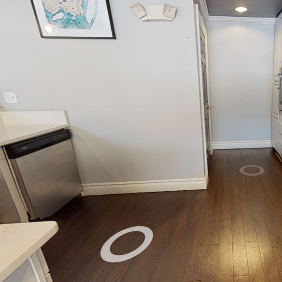 A kitchen with wooden floors, white cabinetry, stainless steel appliances, and circular markers on the floor.