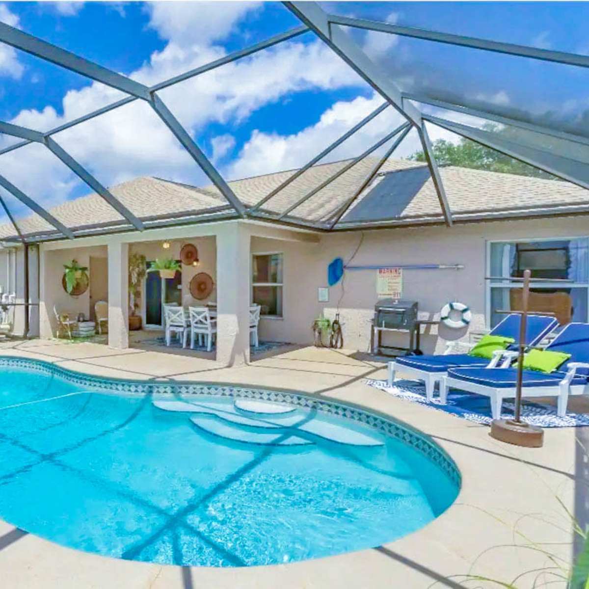 A backyard swimming pool is enclosed by a screened patio, with lounge chairs and a seating area visible in a well-lit setting.