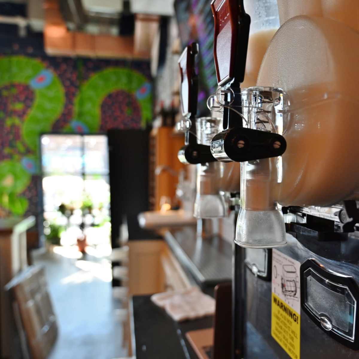 A close-up of drink dispensers on a counter with a colorful, patterned wall in the background.
