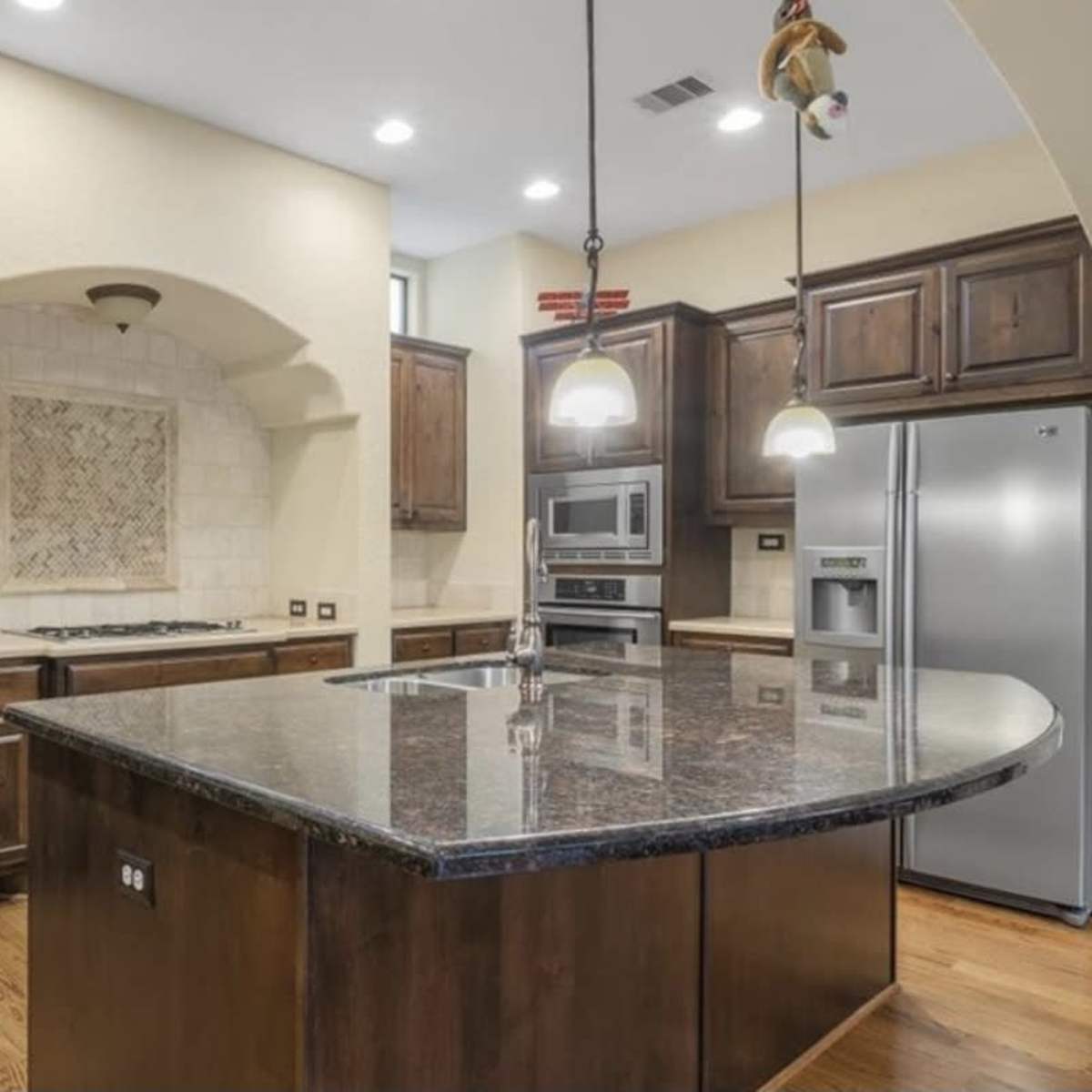 A modern kitchen with dark wooden cabinetry, a large granite island, and stainless steel appliances.