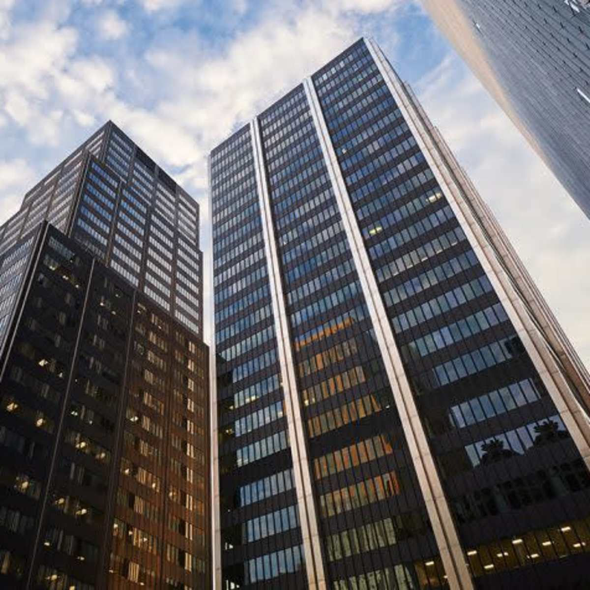 Tall office buildings rise against a cloudy sky in an urban setting.