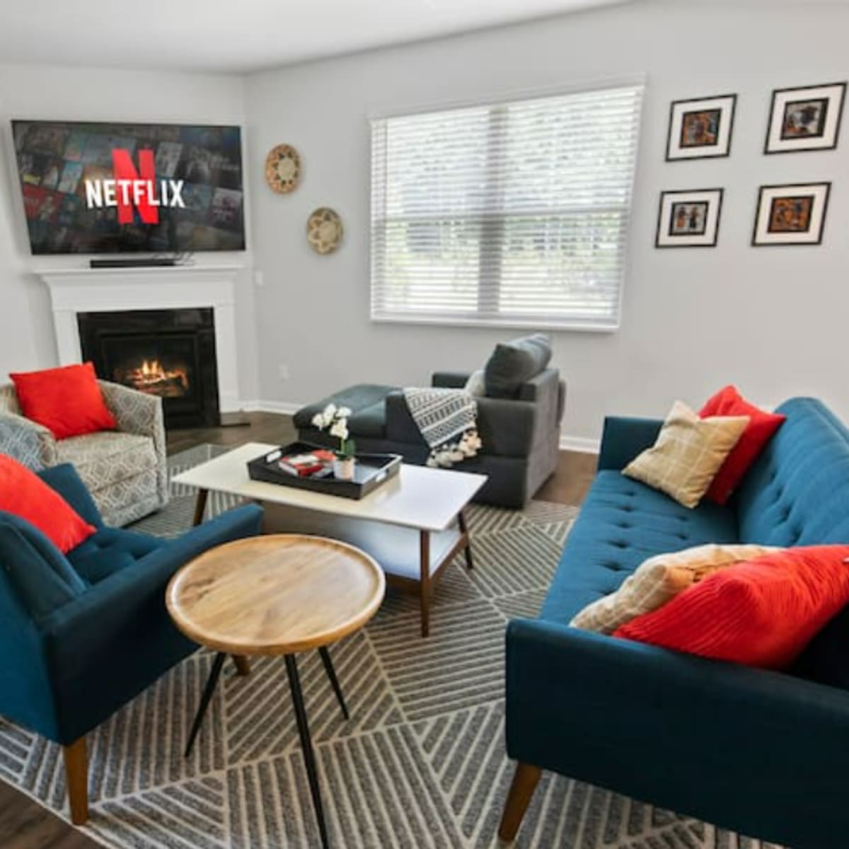 The living room features a fireplace, a large TV displaying the Netflix logo, and blue sofas arranged around a coffee table with decorative accents.