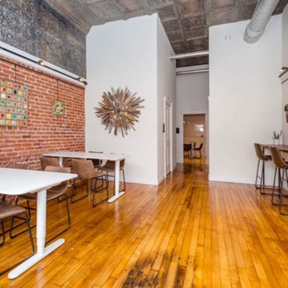 A cozy cafe interior featuring exposed brick walls, wooden floors, and modern tables with chairs.