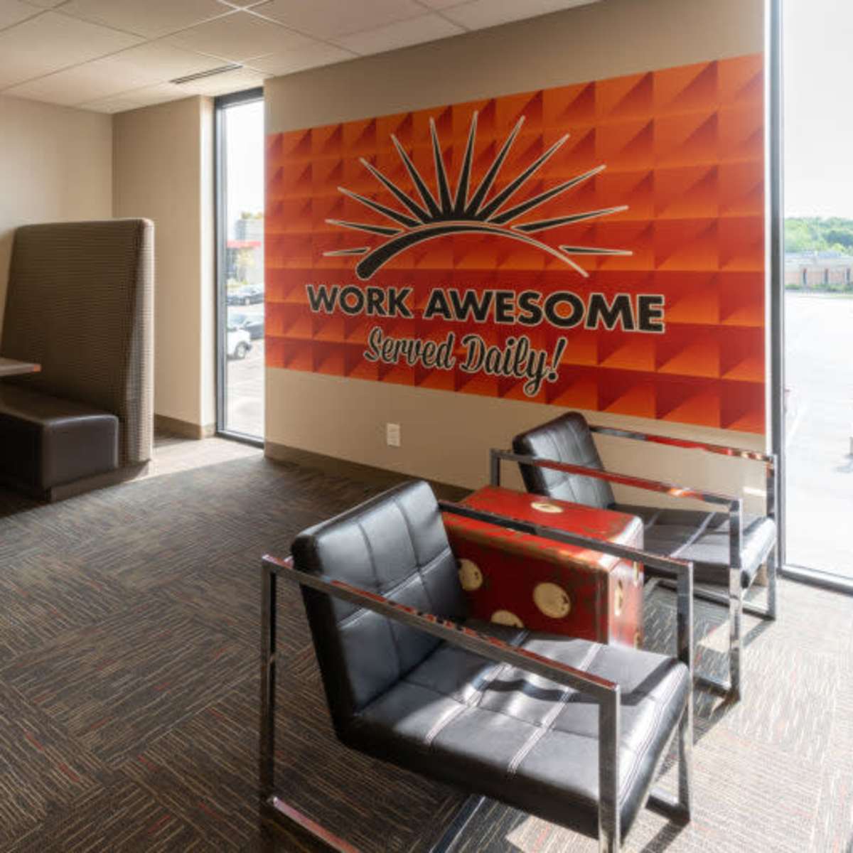 A modern workspace with seating arrangements, a large wall mural that reads "WORK AWESOME Served Daily!", and a small desk with a television set.