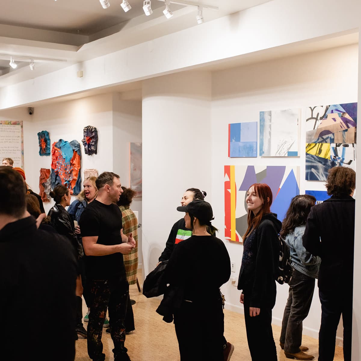 A diverse group of people gathers in an art gallery surrounded by abstract paintings and colorful artworks.