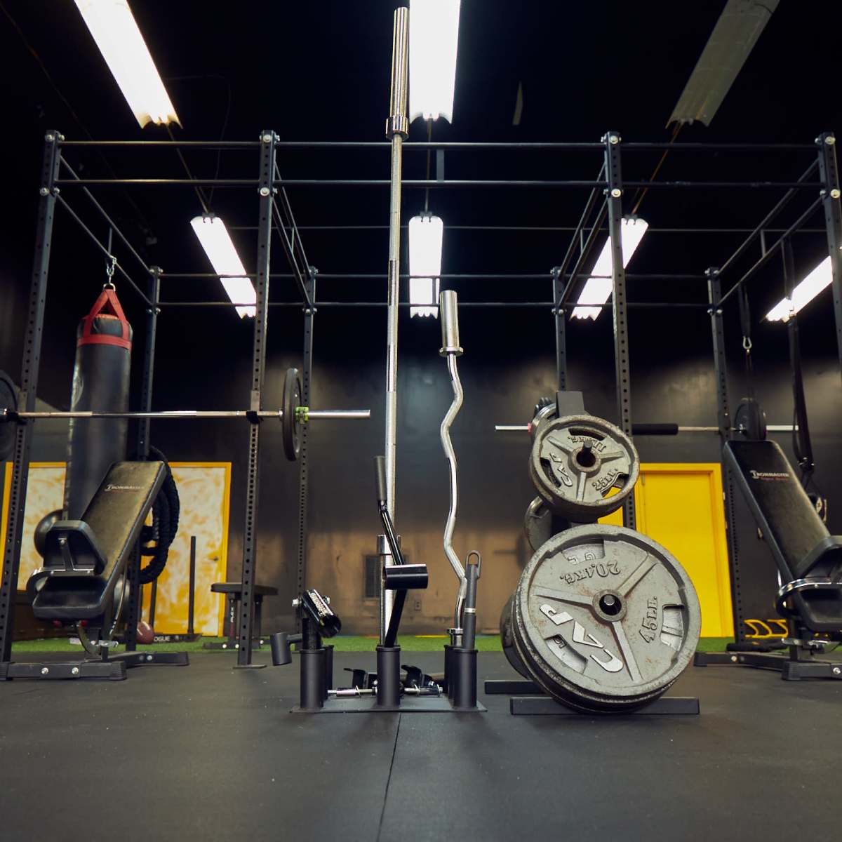A gym facility with various strength training equipment, including weights and a punching bag, under overhead lights.