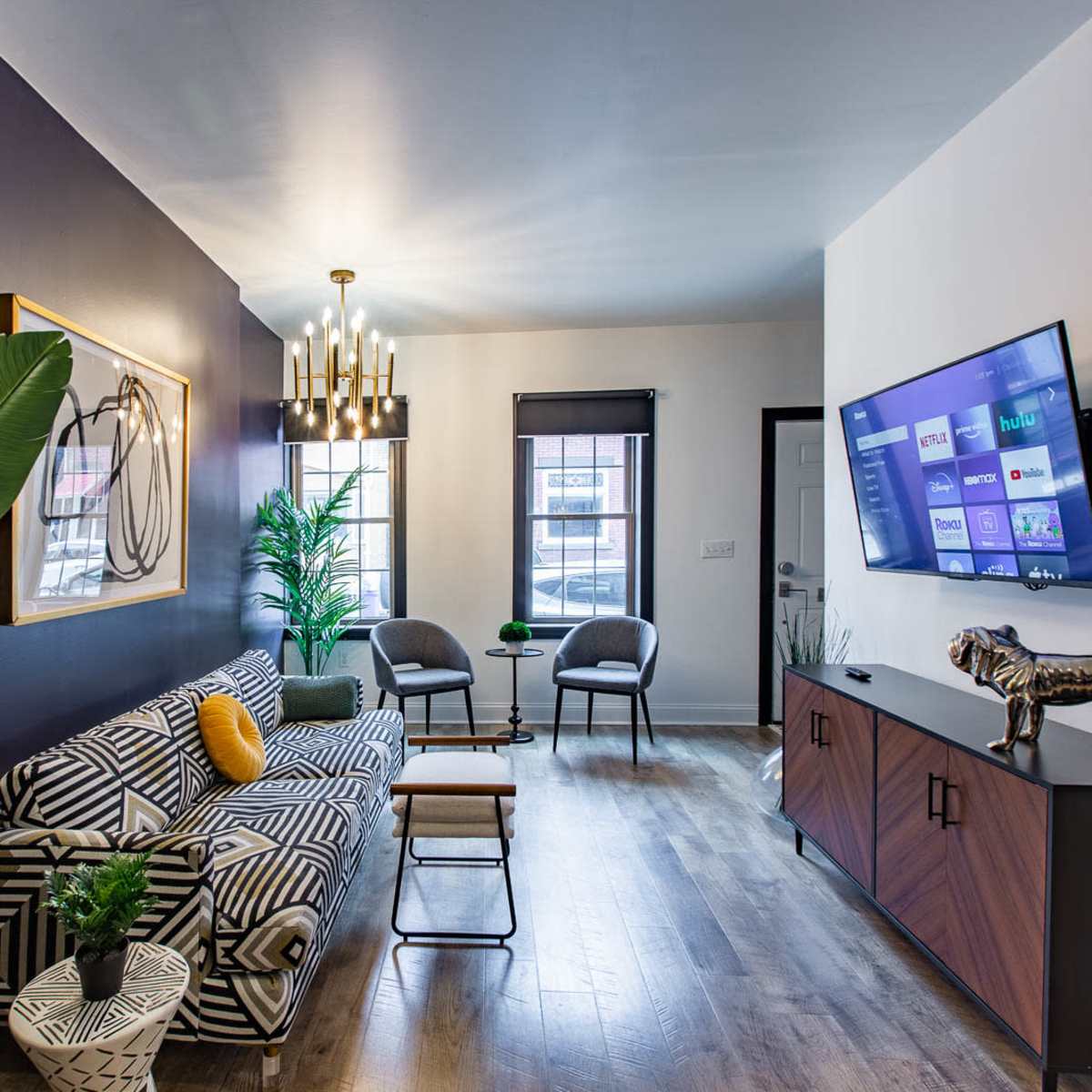 A modern living room with a striped sofa, a coffee table, a television mounted on a wall, and decorative plants.