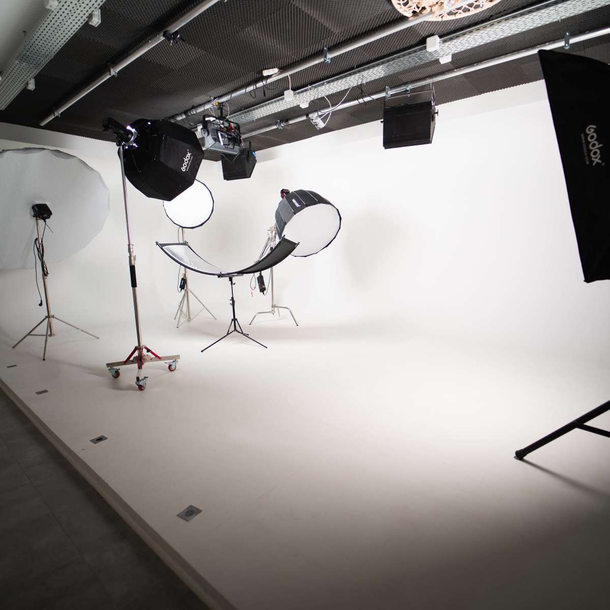 A photography studio with a plain white backdrop, lighting equipment, and a curved chair set up in the center.