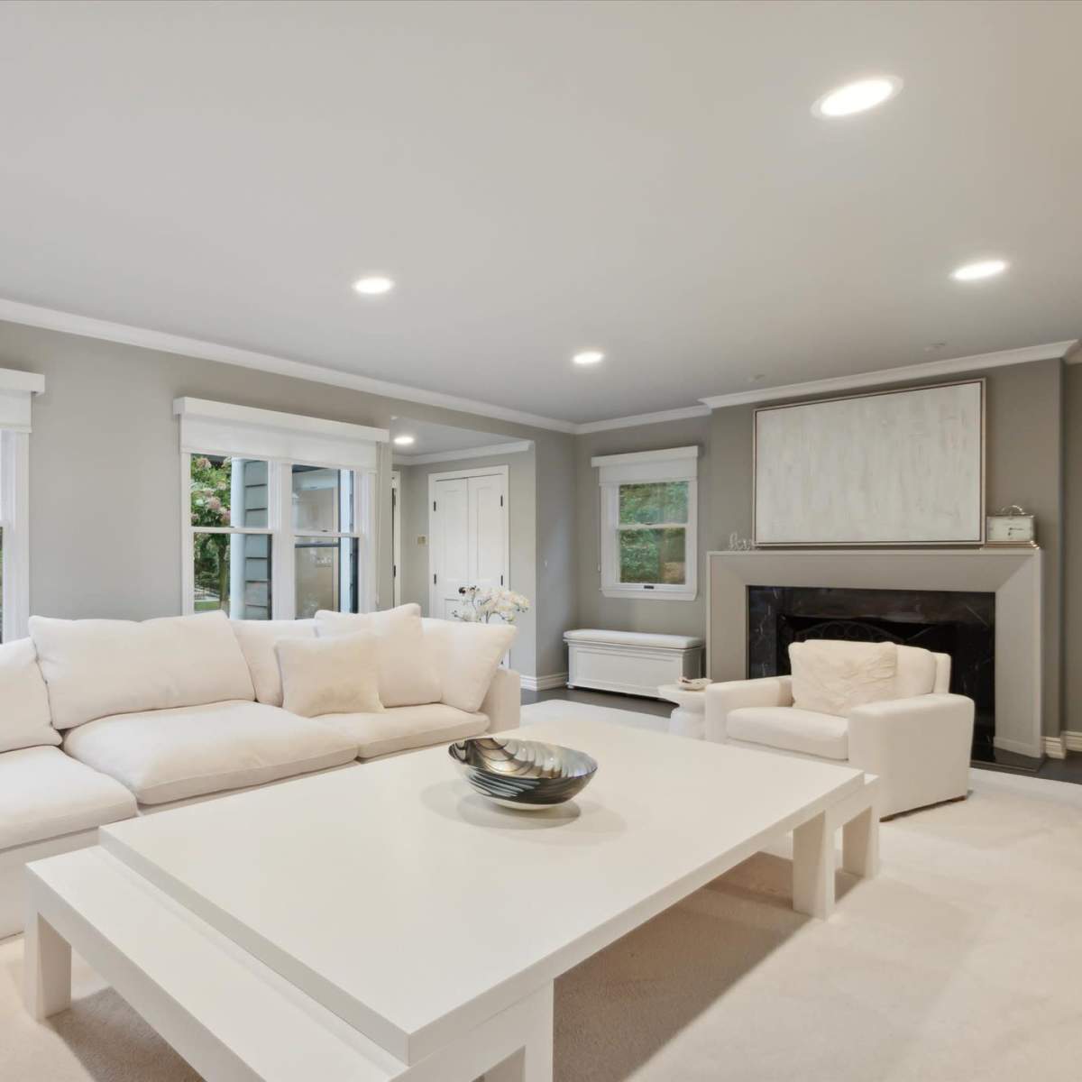 A modern living room featuring a large white sectional sofa, a coffee table, and a fireplace, with natural light coming through the windows.