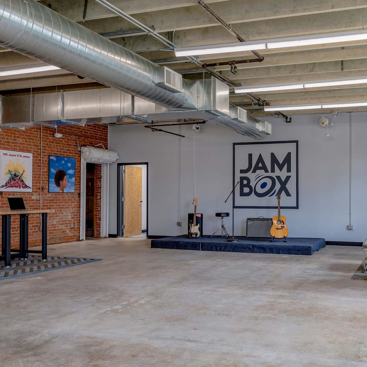 An open space with a stage, a guitar, seating options, and colorful artwork on the walls.