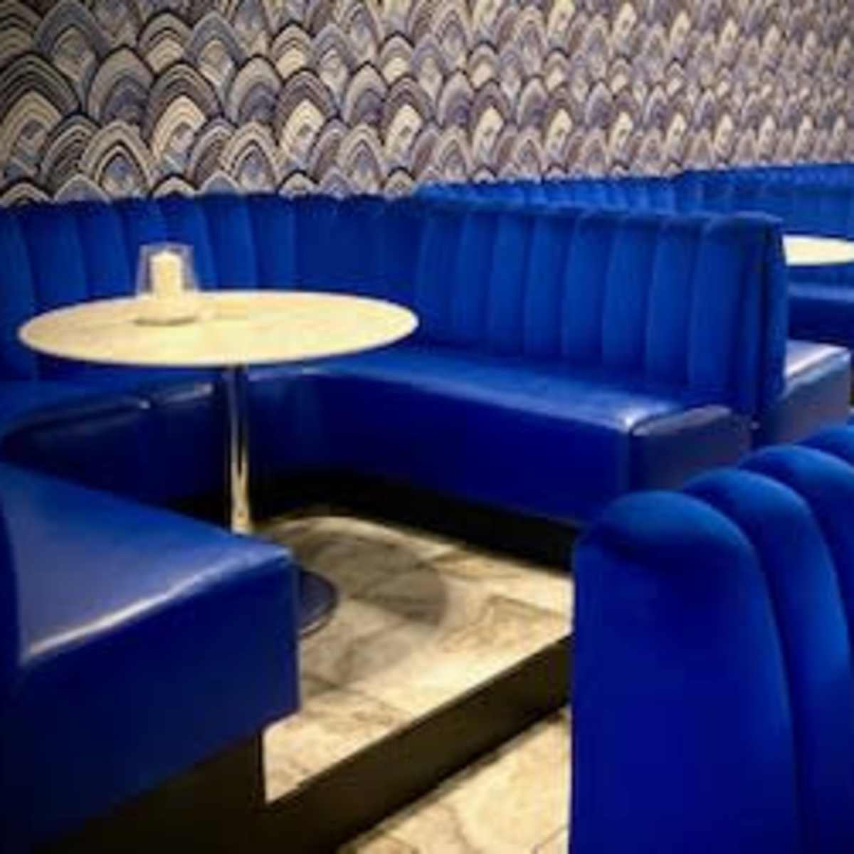 A restaurant interior with blue upholstered booths and circular tables against a patterned wall.