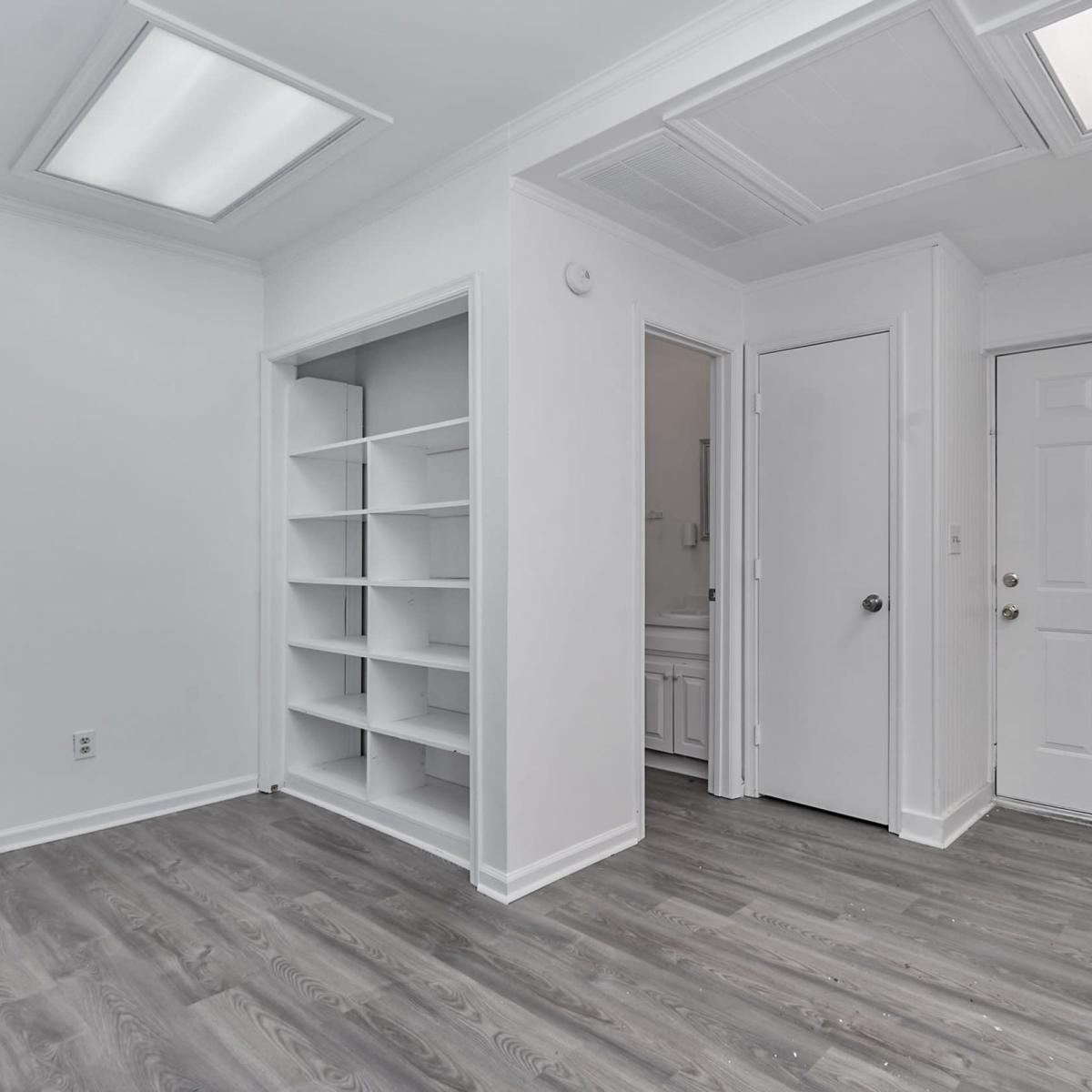 A minimalist interior space with a white wall, a door on the right, and a built-in bookshelf on the left.