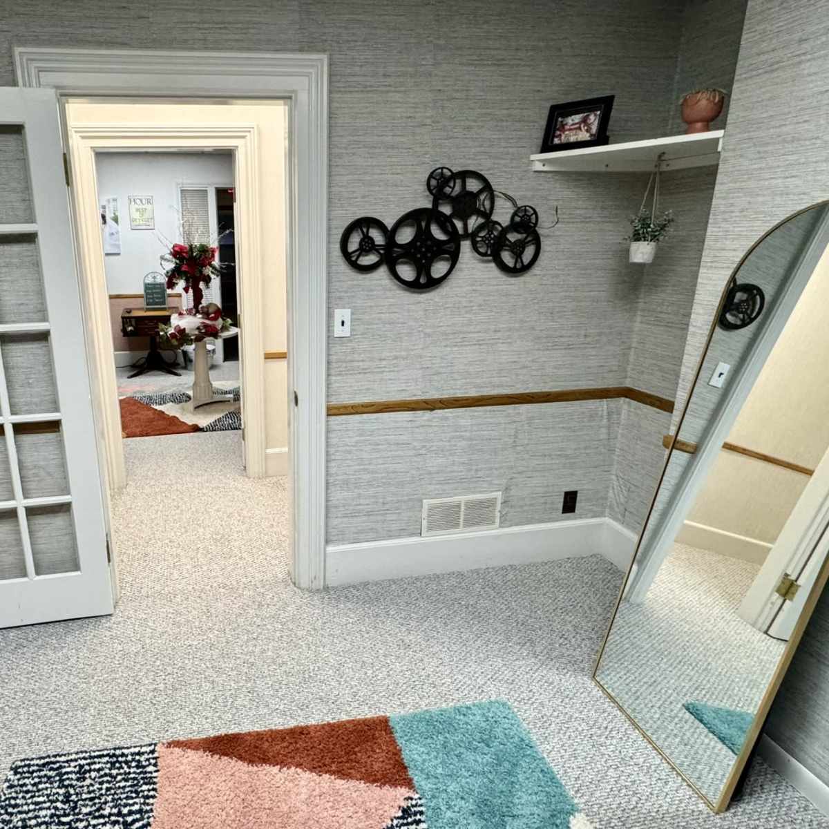 A softly lit room with a green velvet couch, an ornate mirror, and a doorway leading to another room, all accented by patterned rugs and decorative wall elements.