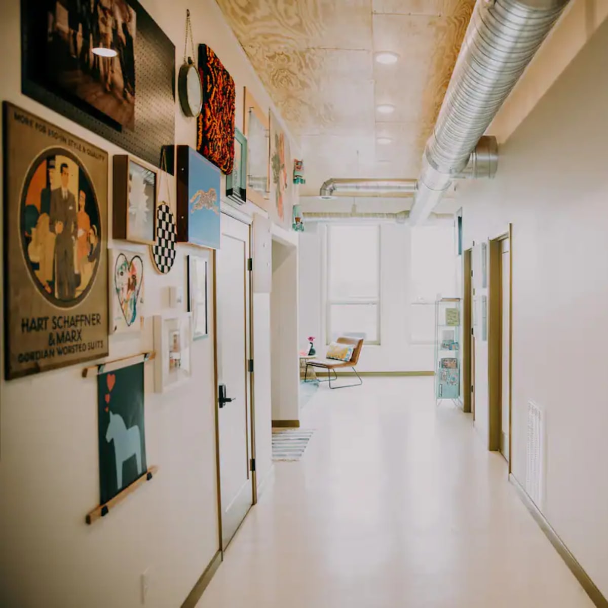 A long hallway features framed artwork on the walls, with doors leading to rooms and large windows at the far end.