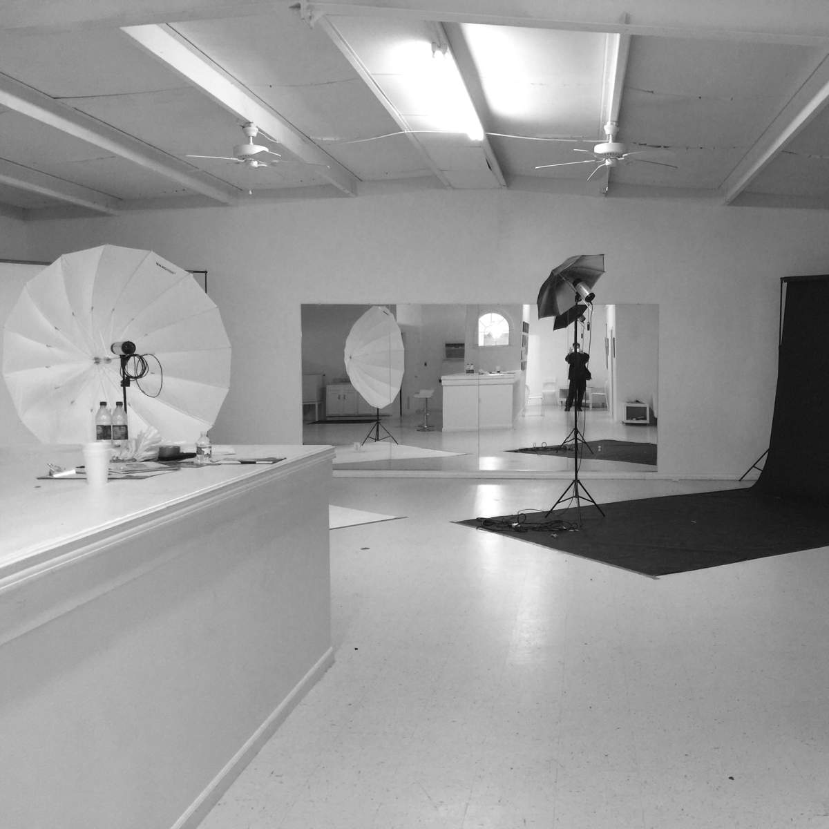 A photography studio features softbox lights, a black backdrop, and large mirrors reflecting the setup.