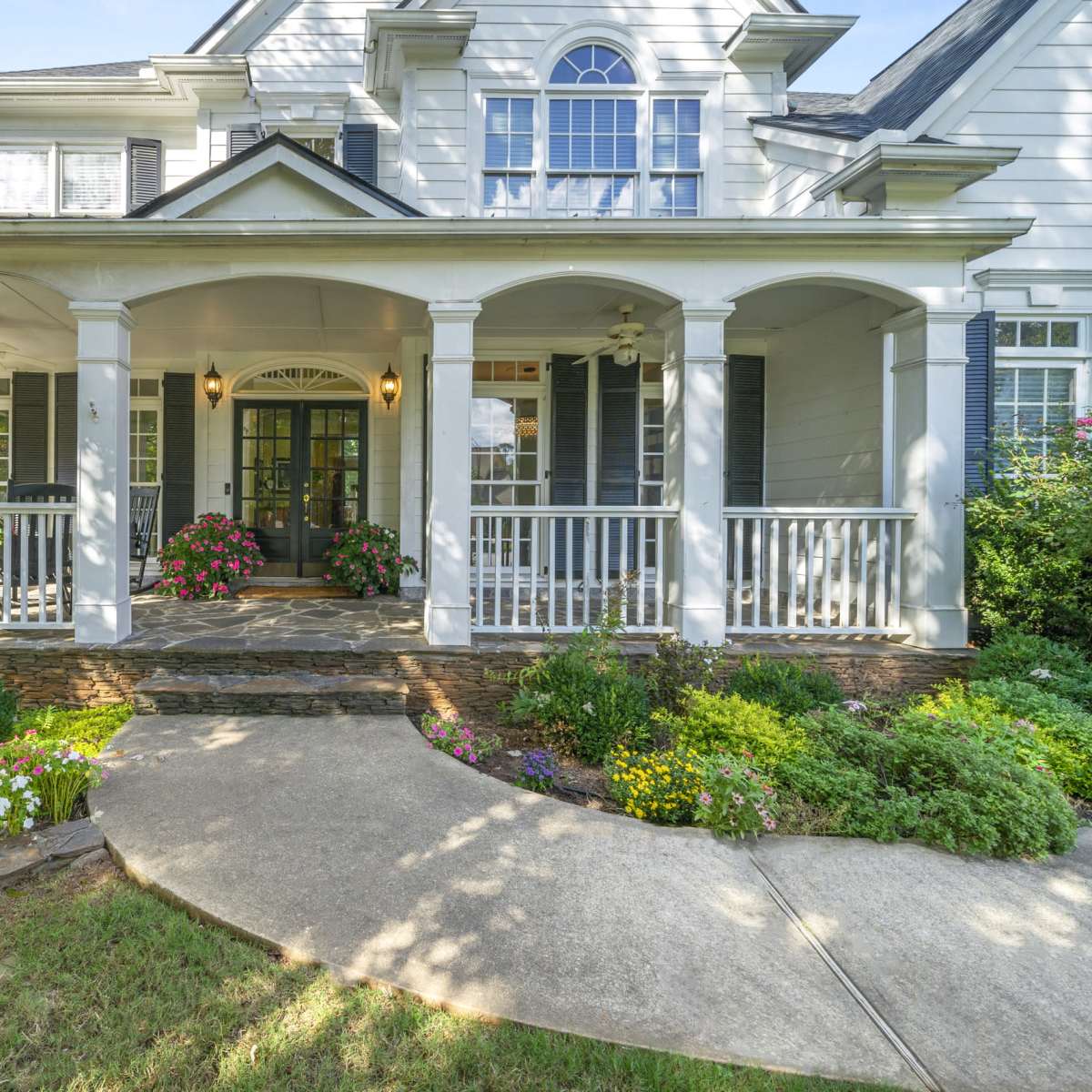 A two-story house with a covered front porch, stone walkway, and landscaped flower beds.