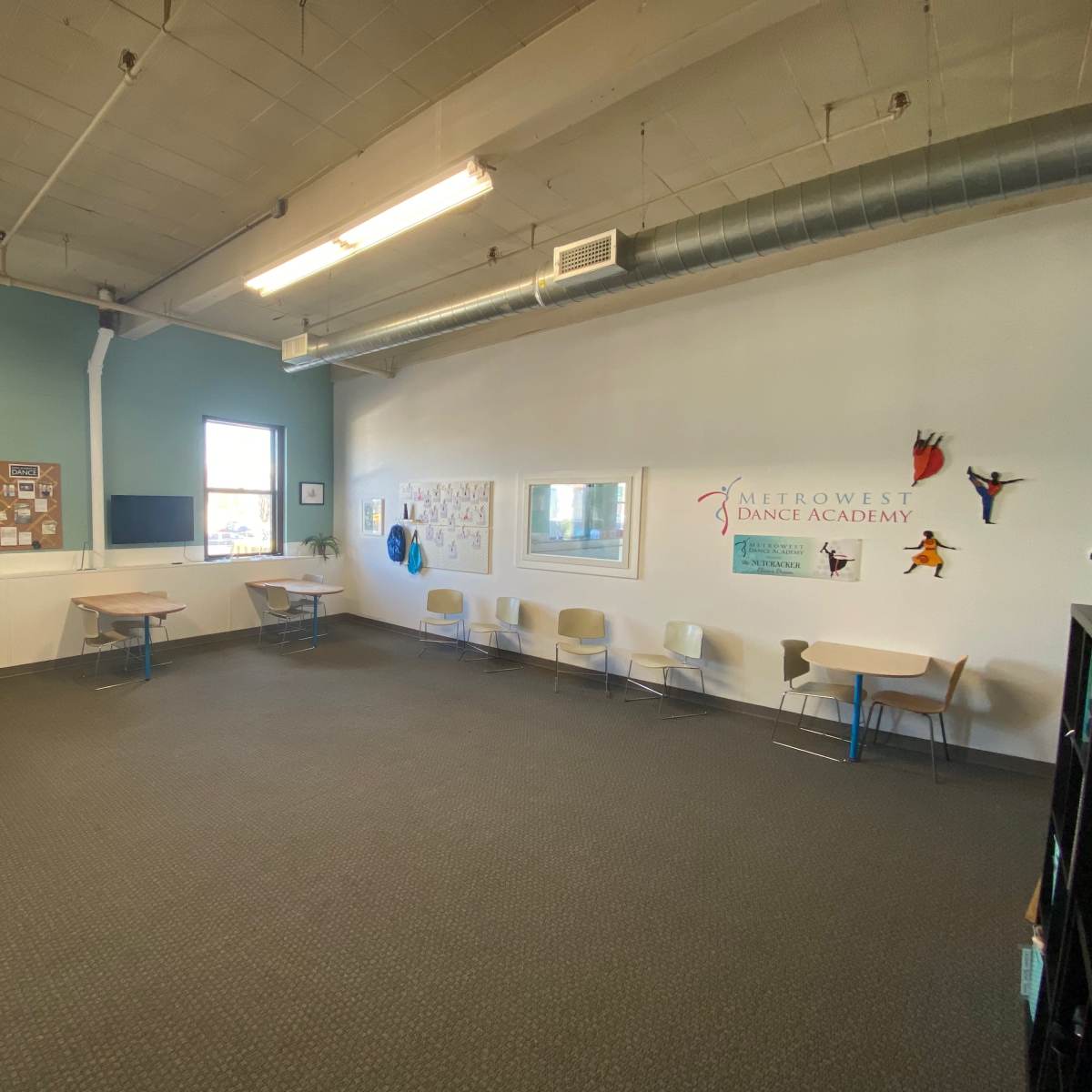 A spacious, well-lit dance studio with several tables and chairs arranged along the walls.