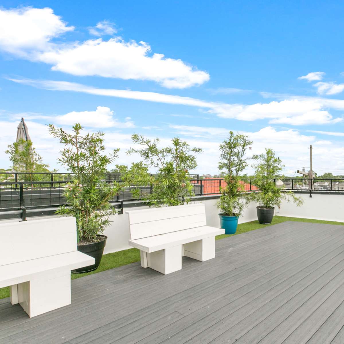 A rooftop deck with white benches, potted plants, and a seating area surrounded by a clear blue sky.