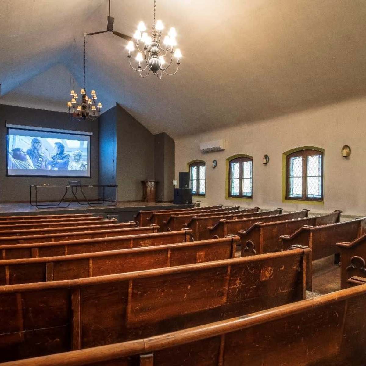 A sparsely filled auditorium with wooden benches facing a projection screen at the front.