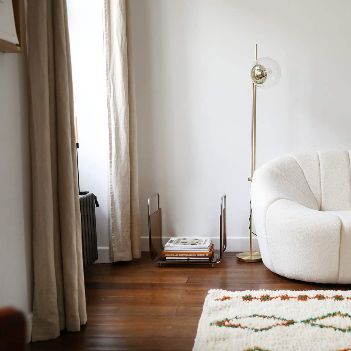 A modern living room featuring a curved white sofa, a wooden coffee table, a floor lamp, and a textured area rug.