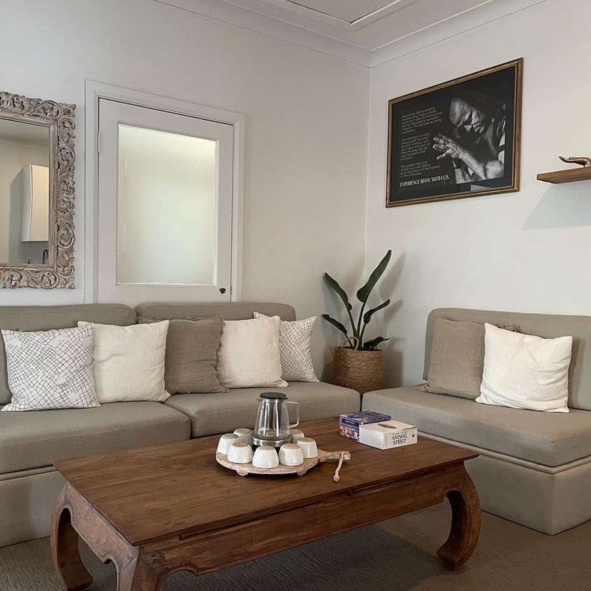 A cozy living room with a beige sectional sofa, a wooden coffee table, and a decorative mirror on the wall.
