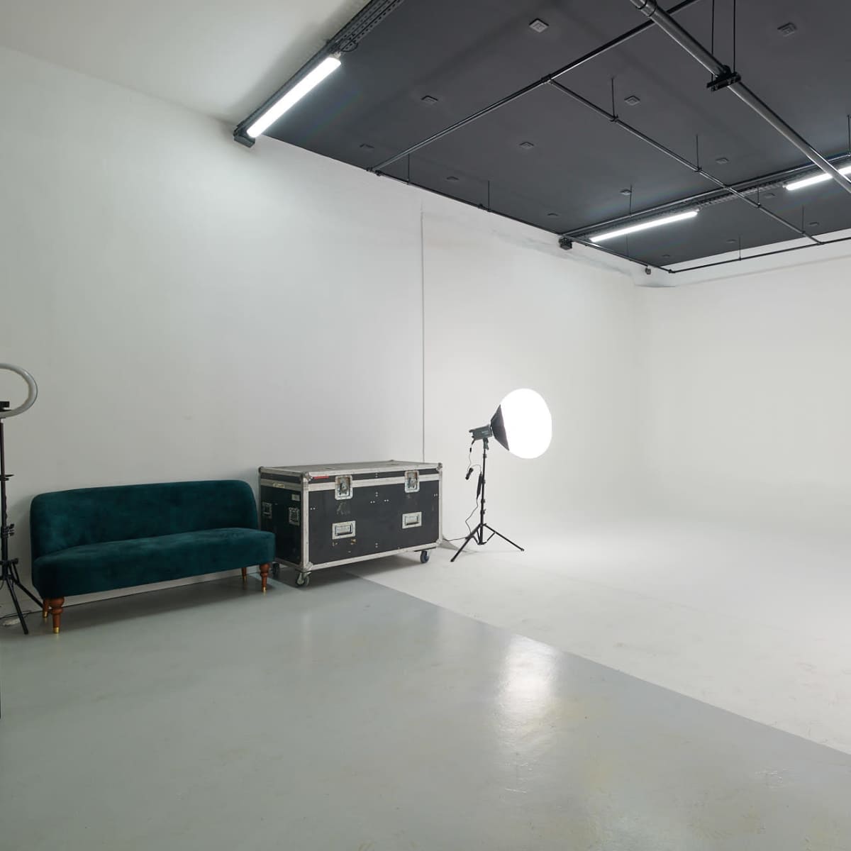 A minimalistic photo studio features a white backdrop, two light setups, and a green velvet sofa on one side.