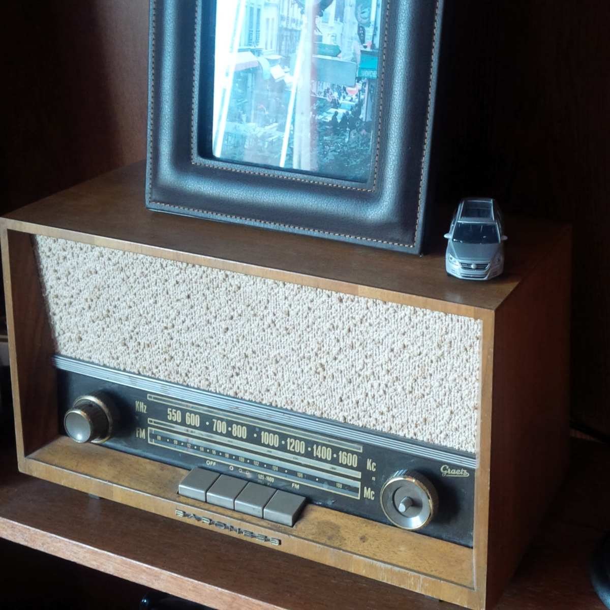 A vintage radio sits on a shelf alongside a framed photograph, a small toy car, and a classic microphone.