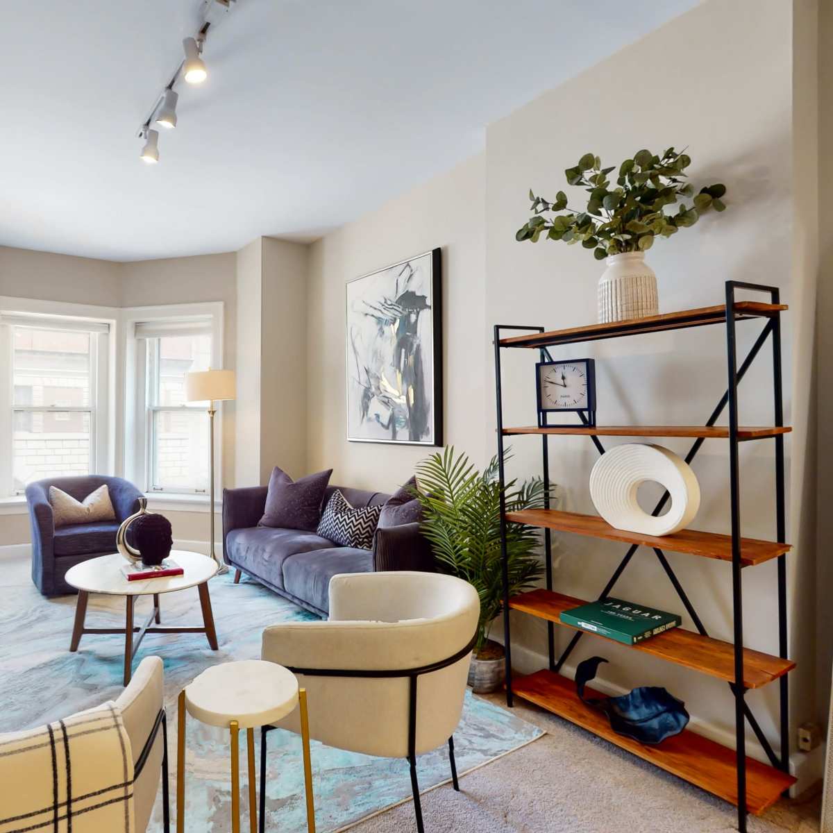 A cozy living room featuring a sofa, armchairs, a coffee table, a television, and decorative plants in a sunlit space.
