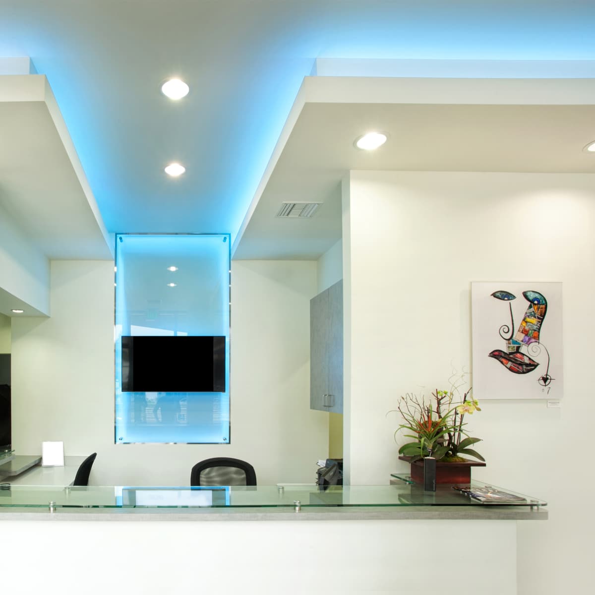 A brightly lit reception area features a glass countertop, modern decor, and artwork on the walls.