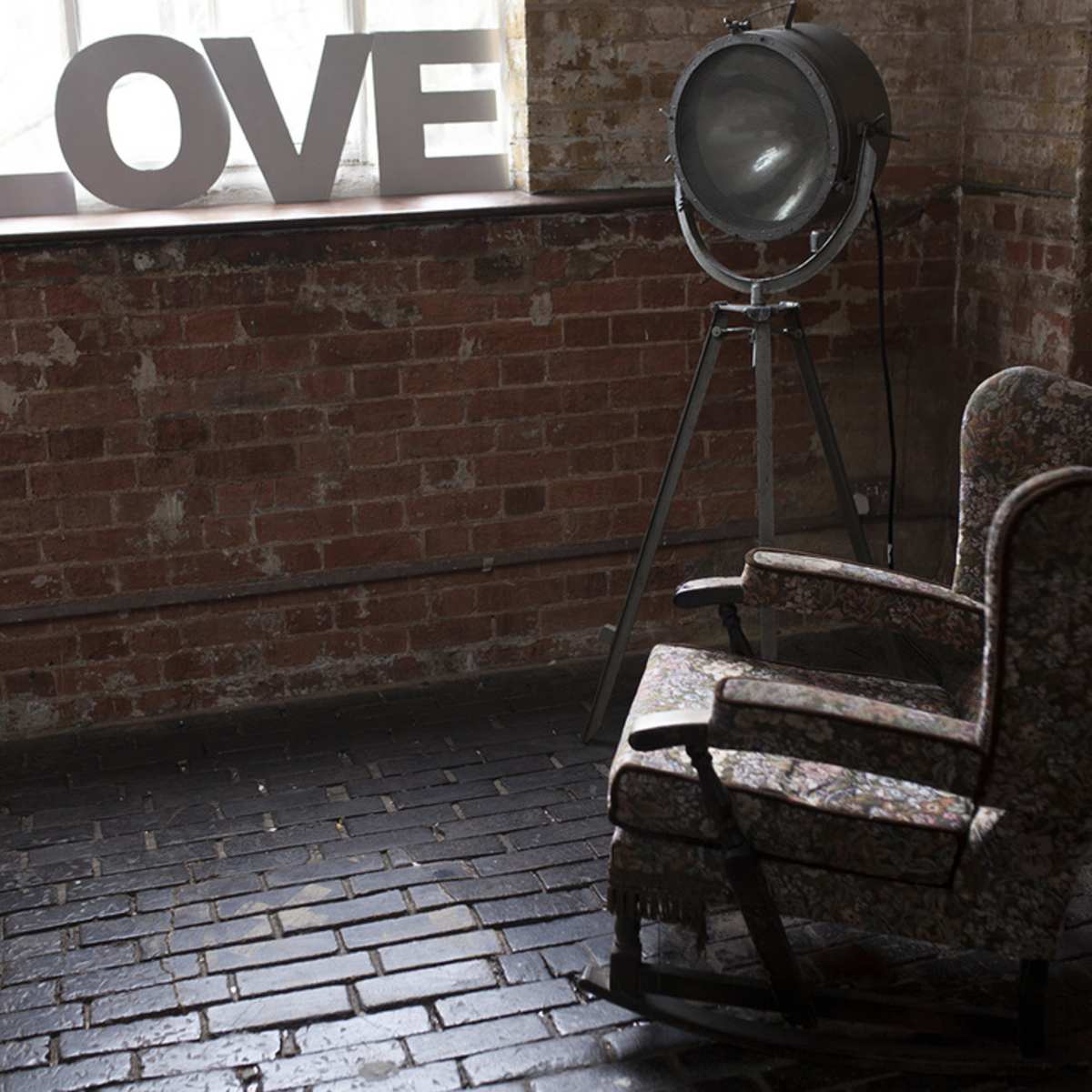 Two vintage floral armchairs beside a large, industrial light and the word "LOVE" displayed in capital letters on a brick wall.