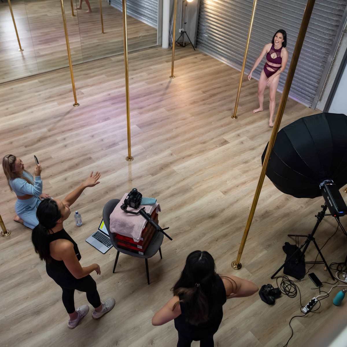 A studio with four women, two standing near a pole while one is sitting behind a camera, and another is gesturing from the side.