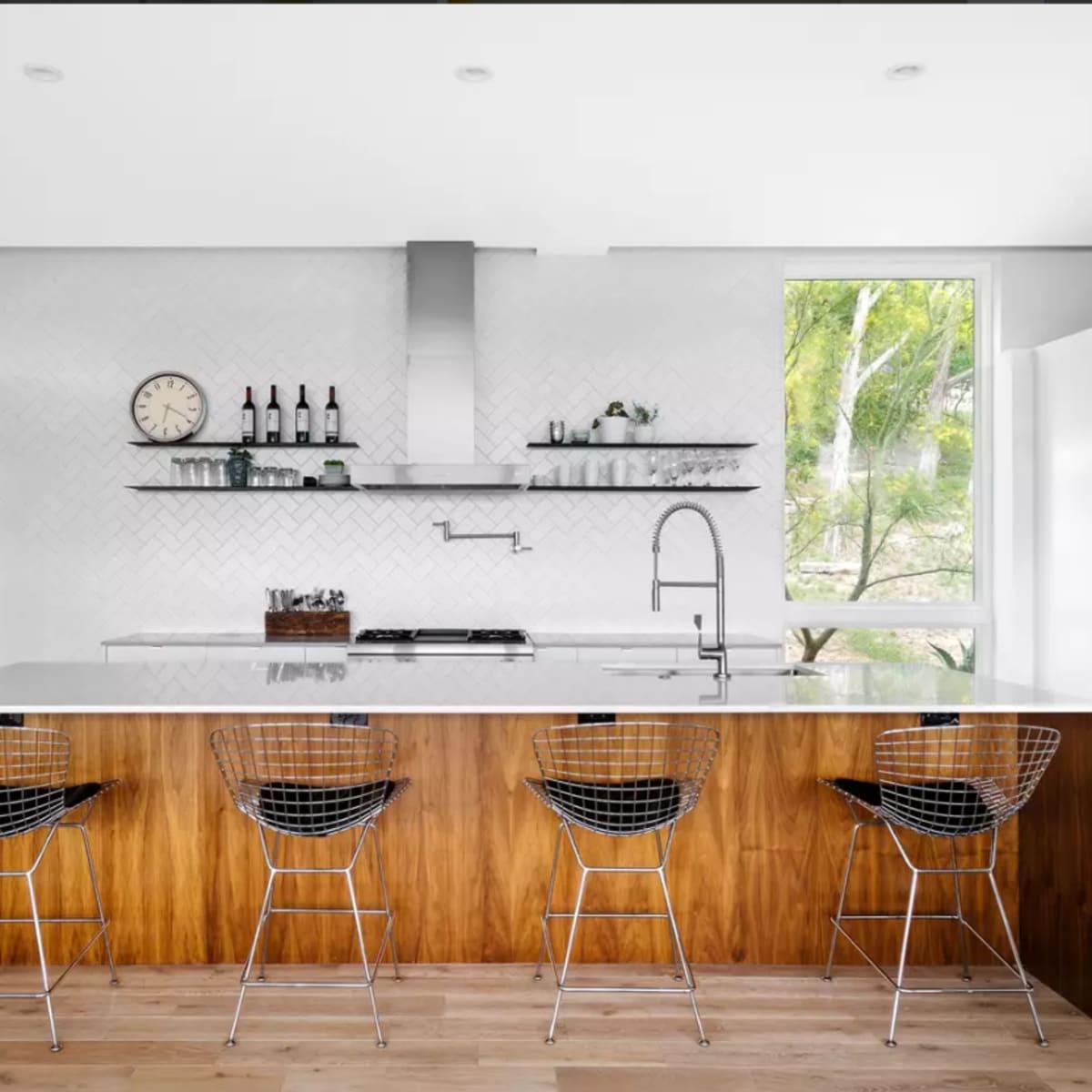 A modern kitchen featuring a large island with wooden accents, sleek stainless steel appliances, and wire bar stools.