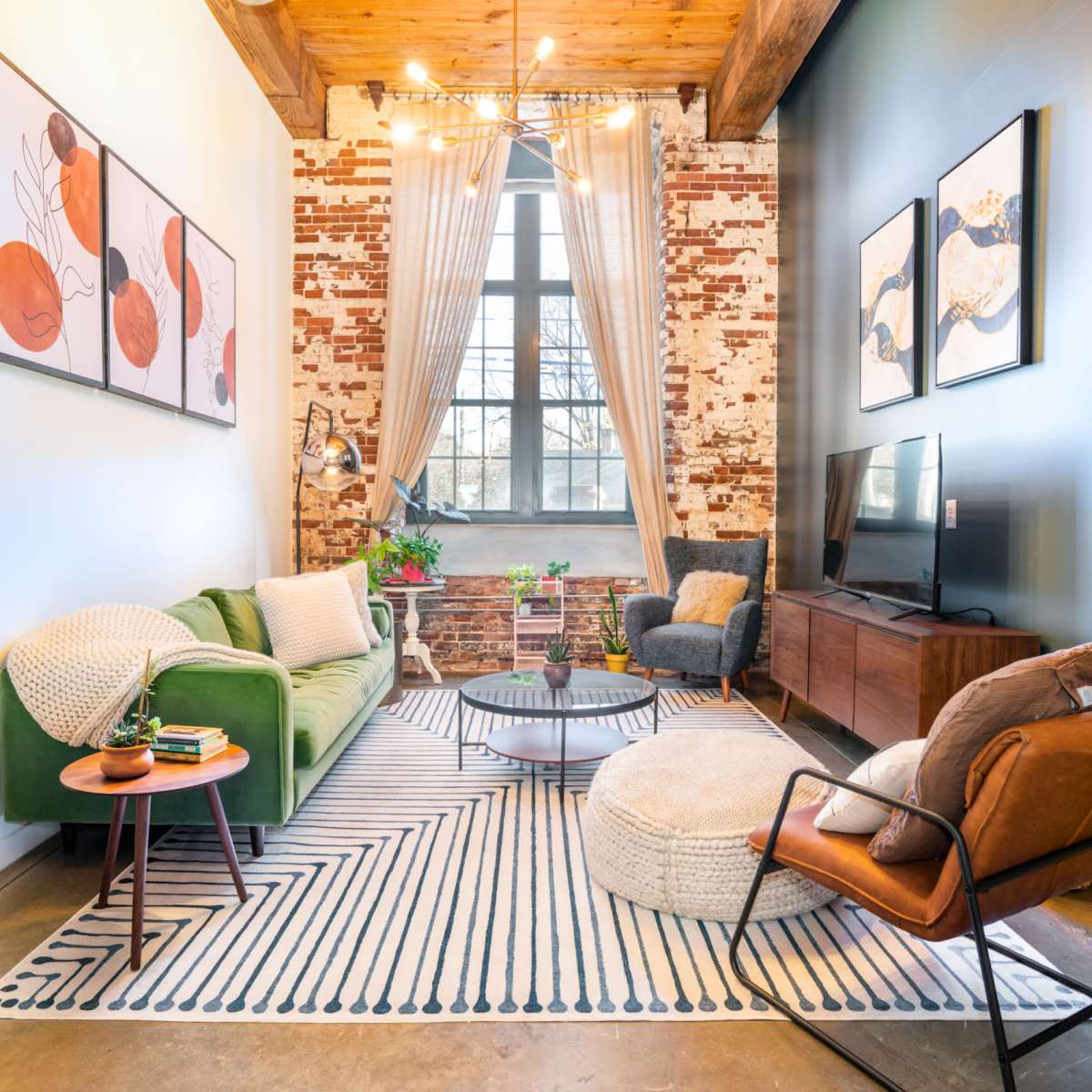 A cozy living room featuring green and brown seating, a round coffee table, an area rug with a striped pattern, and exposed brick walls.