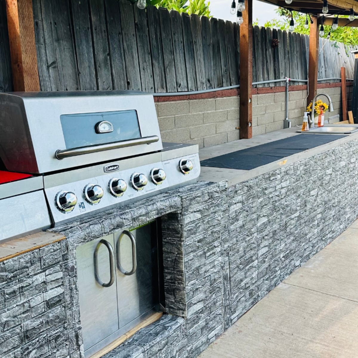 An outdoor kitchen featuring a stainless steel grill and a stone countertop with a cabinet underneath.