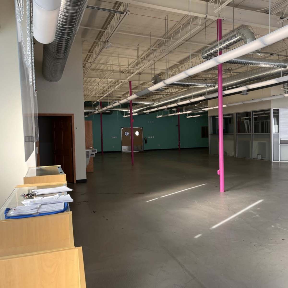 An empty commercial space with large windows, exposed ductwork, and pink pillars supporting the ceiling.