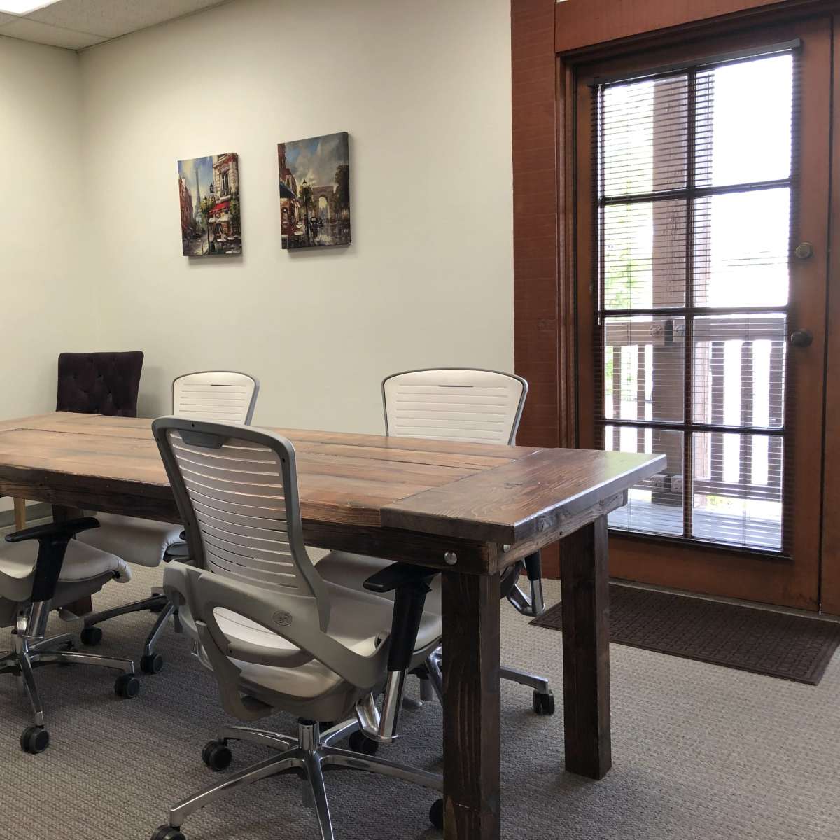 A modern conference room with a wooden table surrounded by four ergonomic chairs, and a door leading to an exterior deck.
