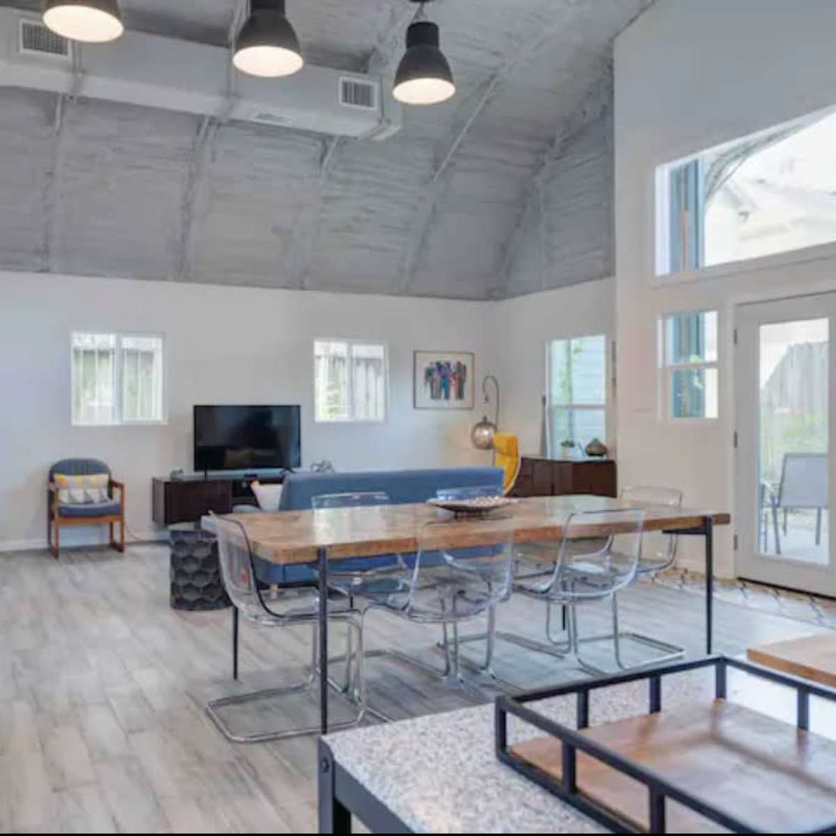 A spacious, modern living area featuring a large dining table, a television, and large windows that provide natural light.
