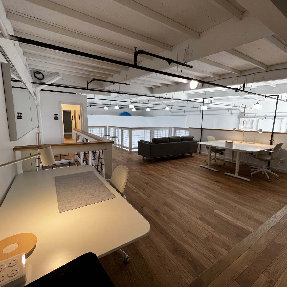 A spacious, modern office environment featuring desks, a couch, and wooden flooring.