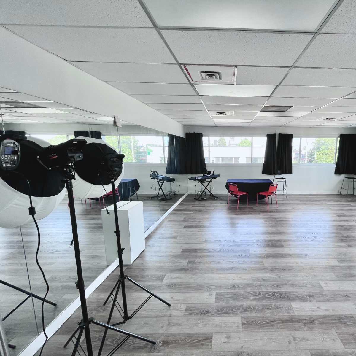 An empty studio space with a wooden floor, large windows, and equipment set up for photography or video production.