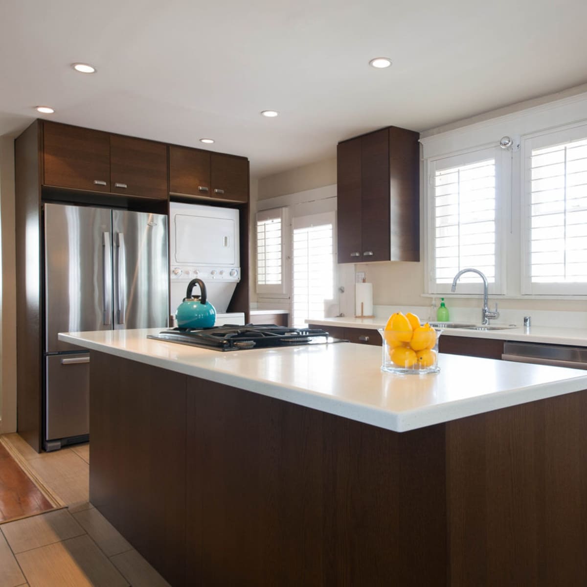 A modern kitchen featuring dark wood cabinetry, a central island with a white countertop, and stainless steel appliances.