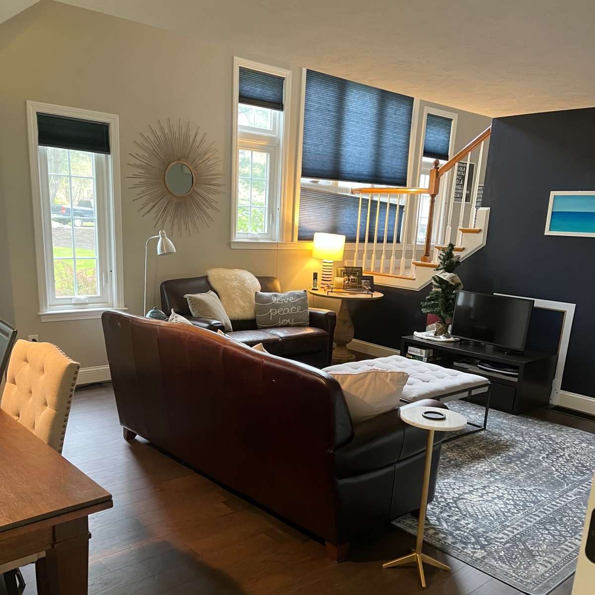 A cozy living room with a dark sofa, a light-colored armchair, a coffee table, and large windows letting in natural light.