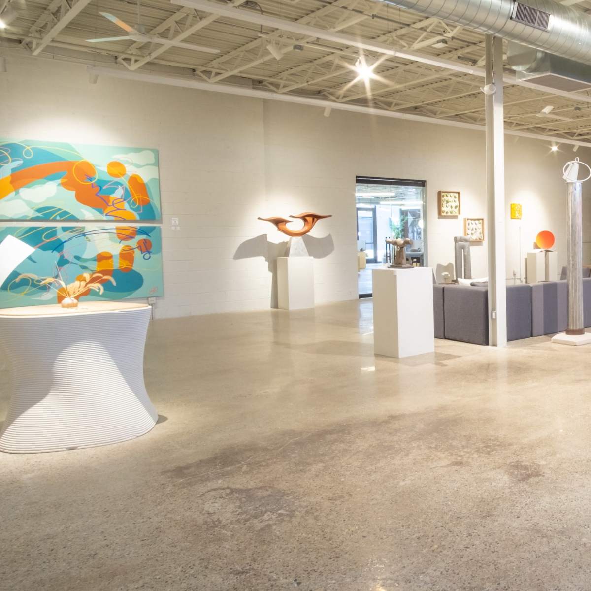 A spacious art gallery featuring various sculptures and artwork displayed throughout a polished concrete-floored interior.